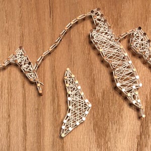 May include: A mountain range string art piece. White string is stretched between small copper nails, creating the outline of mountains. The artwork is mounted on a wooden background.