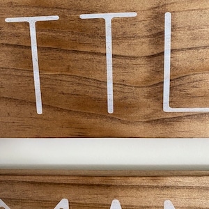 Puede incluir: Una vista de cerca de dos tablones de madera apilados con un acabado de grano de madera marr&oacute;n natural. El tabl&oacute;n superior presenta las letras blancas T, T y L, mientras que el tabl&oacute;n inferior muestra las letras blancas M, A y N en fuente.