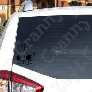 May include: A black vinyl decal of the Mudkip character applied to the rear window of a white vehicle. The graphic features the creature's distinct head fin, wide cheeks, and four-legged stance, rendered in a simple, solid black outline style.