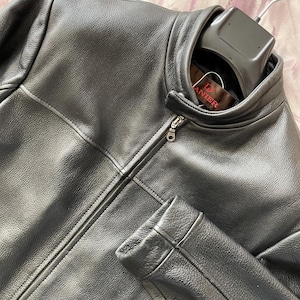 May include: A black leather jacket with a zip-up front and a stand-up collar. The jacket has a smooth texture and is hanging on a black hanger. The brand tag reads "DANIEL".