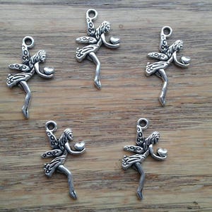 May include: Five silver charm pendants shaped like fairies holding hearts. Each fairy has wings and a flowing dress. The charms are perfect for jewelry making or adding a touch of whimsy to crafts.