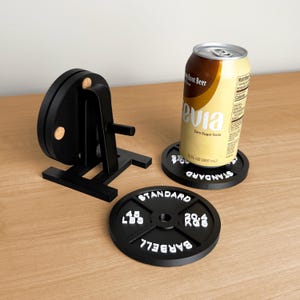 Może przedstawiać: Biały ceramiczny kubek z czarnym uchwytem i napisem "But first, coffee" w stylu ręcznym. Kubek stoi na białej powierzchni. Kubek ma około 10 cm wysokości.