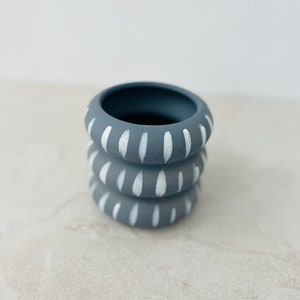 May include: A stack of three gray ceramic planters with white painted designs. The planters are stacked on top of each other and have a simple, modern design.