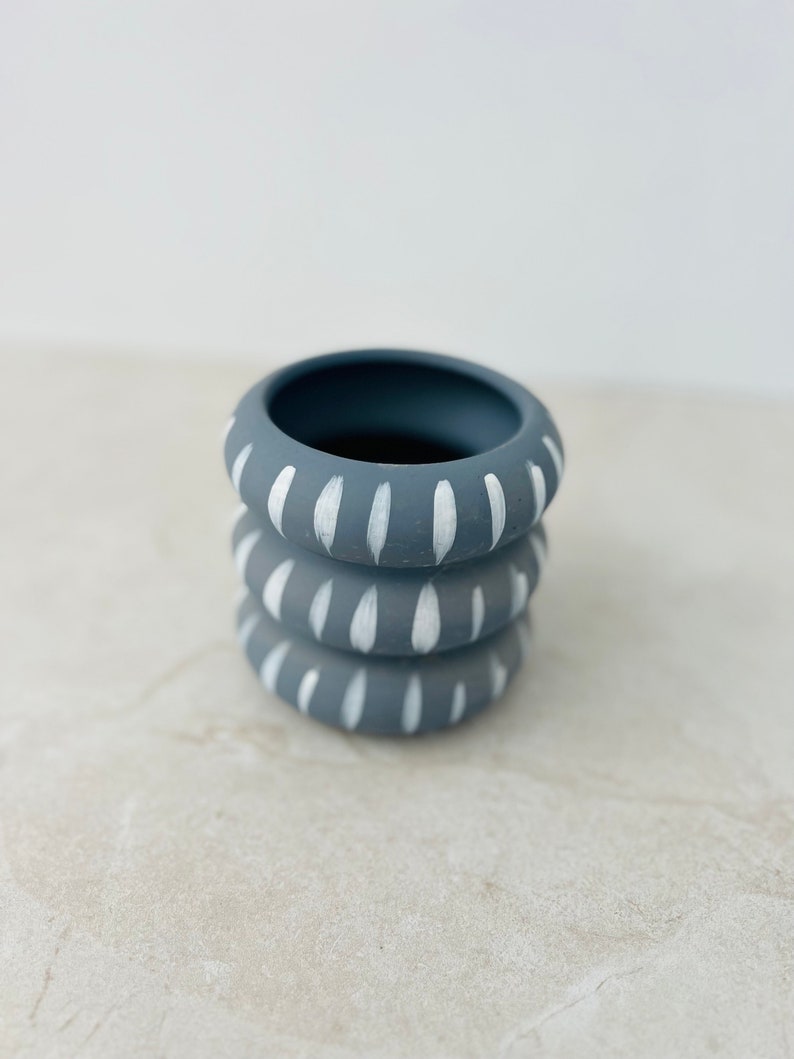 May include: A stack of three gray ceramic planters with white painted designs. The planters are stacked on top of each other and have a simple, modern design.