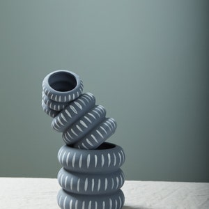 May include: A stack of four gray ceramic planters with white painted lines. The planters are stacked on top of each other and are slightly tilted to the side. The planters have a simple, modern design.