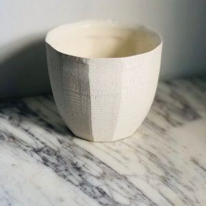 May include: White ceramic planter with a textured surface. The planter has a rounded shape and a wide opening.