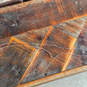 May include: A transparent acrylic template with a curved design, placed on a rustic wooden surface. The template's shape indicates it's for crafting or design, possibly for creating curved edges or patterns. The wood has a mix of brown and orange tones.