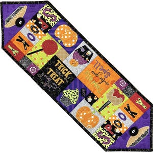 Może przedstawiać: Bieżnik na stół o tematyce Halloween z patchworkowym wzorem. Bieżnik posiada kwadraty z motywami Halloween, takimi jak dynie, cukierki oraz słowa "Spooky" i "Trick or Treat". Krawędzie obramowane są czarno-fioletowym wzorem.