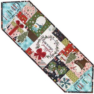 Puede incluir: Un camino de mesa navideño acolchado con un diseño de patchwork. El camino de mesa presenta varios cuadrados con temas navideños con imágenes de regalos, muñecos de nieve y árboles de Navidad. El texto incluye "Tis the season to snuggle!" y "Have a cup of chill."