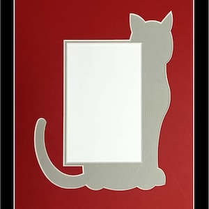 May include: A red mat with a gray silhouette of a cat. The cat is sitting with its back to the viewer and its tail curled around its legs. There is a white rectangle in the center of the mat.