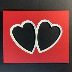 May include: A red card with two white heart-shaped cutouts. The hearts are overlapping and create a unique design.