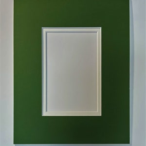May include: A green mat with a white mat opening in the center. The mat is designed to be used for framing artwork or photographs.