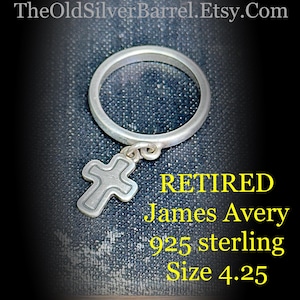 May include: A silver ring with a dangling cross pendant. The ring is marked "RETIRED James Avery 925 sterling Size 4.25". The ring is a religious jewelry item.