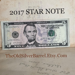 May include: A five dollar bill with a star note designation. The bill is from 2017 and features a portrait of Abraham Lincoln. The serial number is PF 01476971. The bill is in good condition.