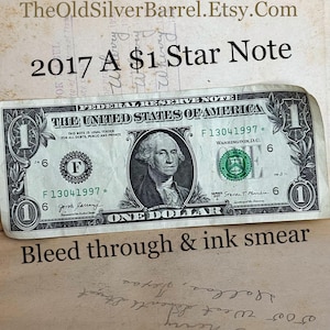 May include: A one dollar bill with a single star on the back. The bill is dated 2017 and has the serial number F13041997. The bill is slightly faded and has some ink bleed through. The text "2017 A $1 Star Note" is visible at the top of the image.