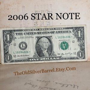May include: A one dollar bill with a portrait of George Washington. The bill is a 2006 star note with the serial number L10394226. The bill is in good condition.