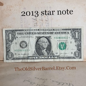May include: A one dollar bill with a portrait of George Washington and the text "THE UNITED STATES OF AMERICA" and "ONE DOLLAR". The bill has a serial number of H02803311 and is dated 2013.