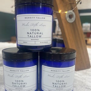 Könnte beinhalten: Drei blaue Glaskerzenbehälter mit schwarzen Deckeln. Jeder Behälter hat ein weißes Etikett mit dem Text "MERRITT TALLOW Made With Love 100% NATURAL TALLOW VANILLA WHIPPED Do not refrigerate".