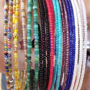 May include: A collection of colorful beaded bracelets in various colors, including black, red, turquoise, green, white, and purple. The bracelets are made of small beads and are stacked together.