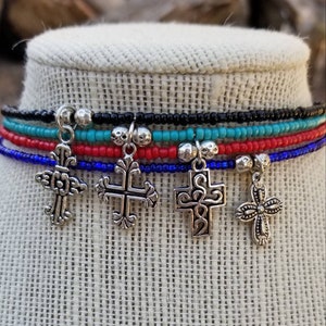 May include: A multi-layered anklet with four silver cross charms. The anklet is made of black, turquoise, red, and blue seed beads.