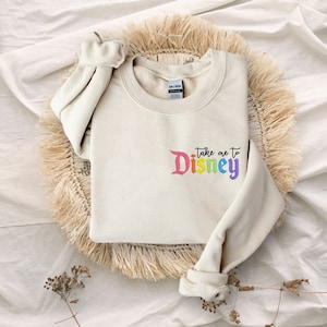 May include: A cream coloured sweatshirt with the text "Take me to Disney" in rainbow colours.