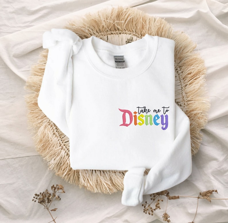 May include: White sweatshirt with a rainbow coloured "Take me to Disney" graphic.