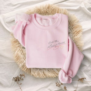 Puede incluir: Una sudadera rosa con el texto "Your pal, Mickey Mouse" en escritura negra con una l&iacute;nea roja debajo y un icono de cabeza de Mickey Mouse amarillo.