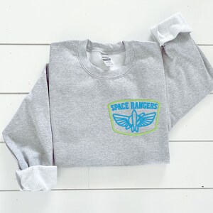 May include: Gray sweatshirt with a blue and green embroidered patch that says "SPACE RANGERS" with a spaceship inside the patch.