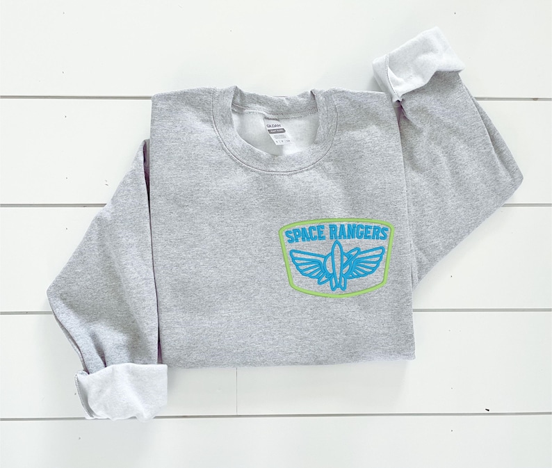May include: Gray sweatshirt with a blue and green embroidered patch that says "SPACE RANGERS" with a spaceship inside the patch.