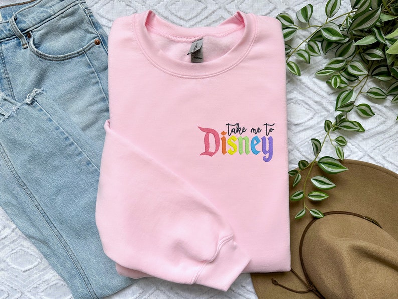 May include: Pink sweatshirt with the text "Take me to Disney" in rainbow colours.