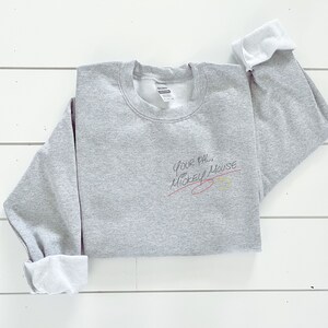 Puede incluir: Sudadera gris con el texto "Your pal, Mickey Mouse" escrito en tinta negra con una l&iacute;nea roja trazada a trav&eacute;s de &eacute;l. Un c&iacute;rculo amarillo con un contorno negro est&aacute; dibujado al lado del texto.