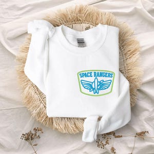 May include: White sweatshirt with a blue and green embroidered patch that says "Space Rangers" with a rocket ship inside.