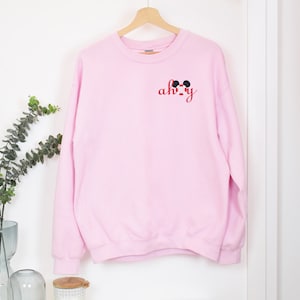 May include: Pink sweatshirt with a red and black Mickey Mouse design and the text "ah-okay" on the front.