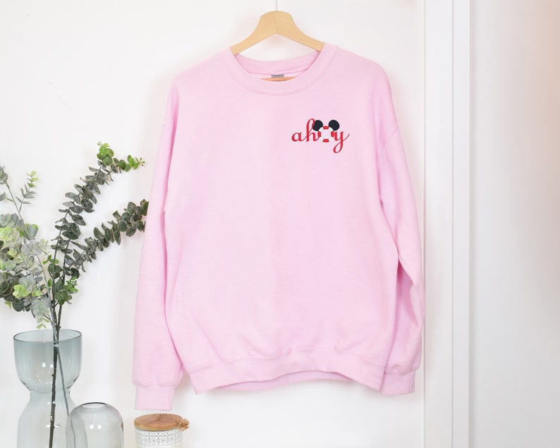 May include: Pink sweatshirt with a red and black Mickey Mouse design and the text "ah-okay" on the front.