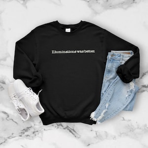 Könnte beinhalten: Schwarzer Pullover mit dem Aufdruck "Illuminations was better." in Weiß auf der Vorderseite. Der Pullover liegt flach auf einer weißen Marmorfläche mit einem Paar weißen Turnschuhen und einer blauen Jeans.