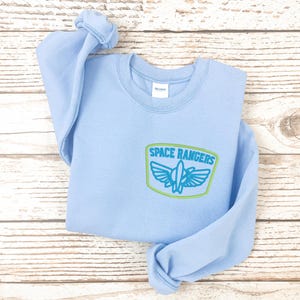 May include: Light blue sweatshirt with a green and blue embroidered patch that says "Space Rangers".