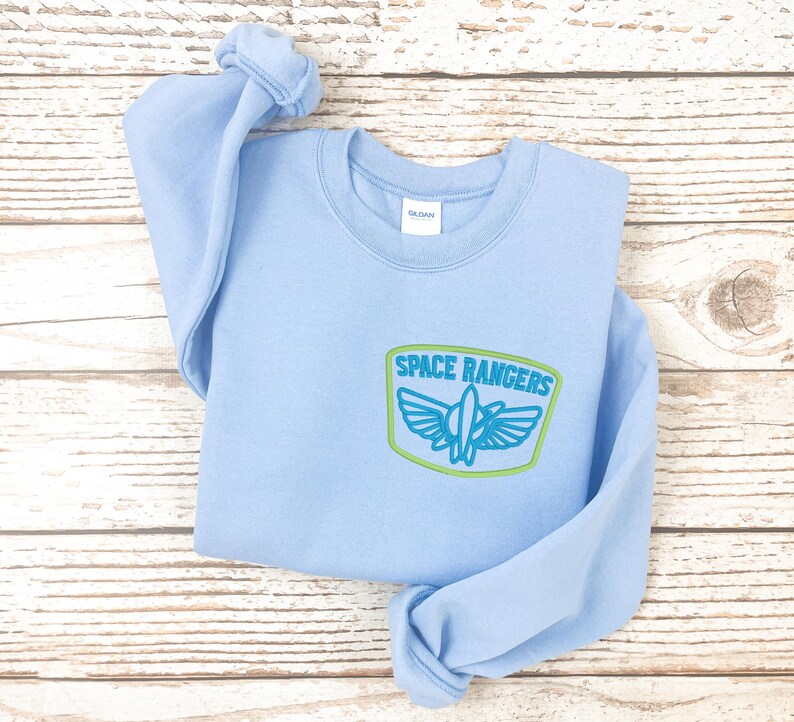 May include: Light blue sweatshirt with a green and blue embroidered patch that says "Space Rangers".