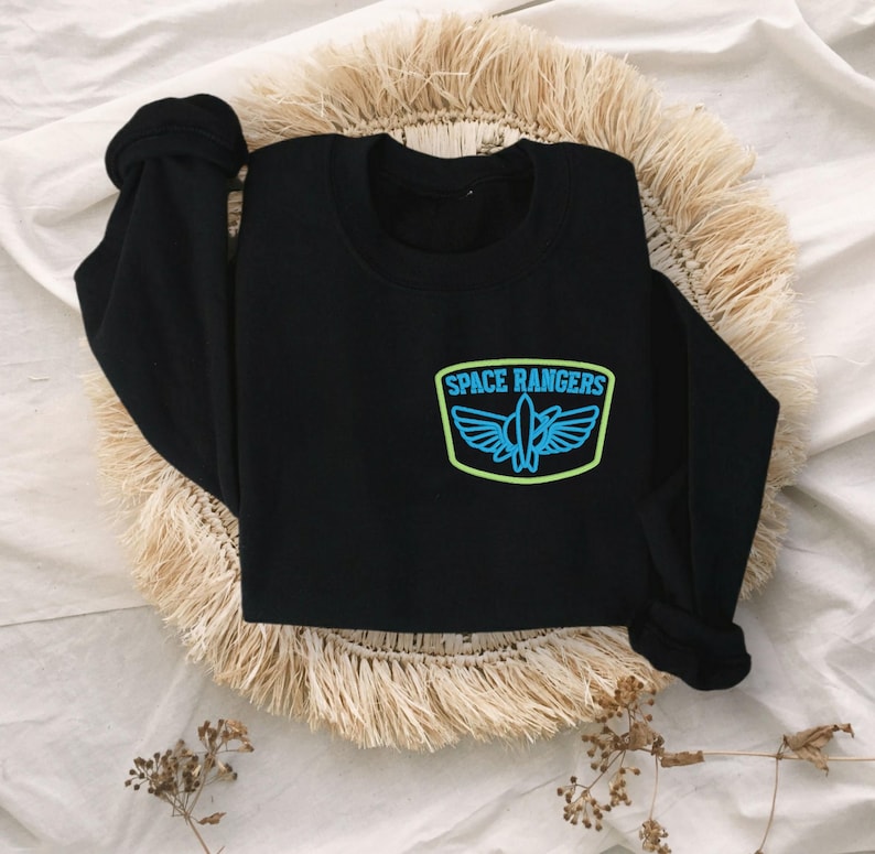 May include: Black long-sleeved sweatshirt with a blue and green embroidered patch that says "SPACE RANGERS" with a spaceship design.