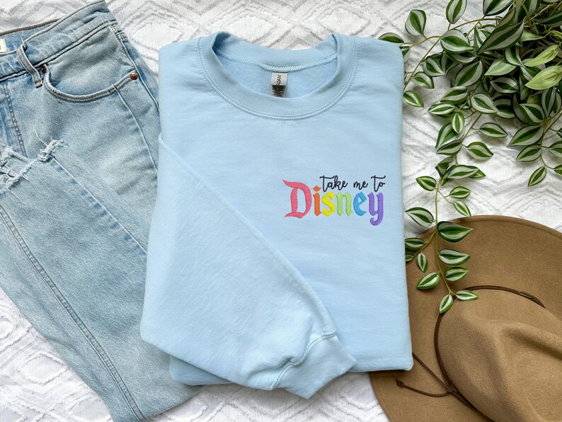 May include: A light blue sweatshirt with the text "Take me to Disney" in rainbow colours.