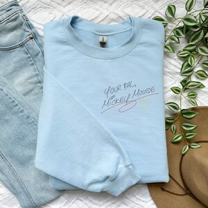 Puede incluir: Sudadera azul claro con el texto "Your Pal... Mickey Mouse" en escritura negra con una l&iacute;nea roja debajo y un icono de cabeza de Mickey Mouse amarillo.