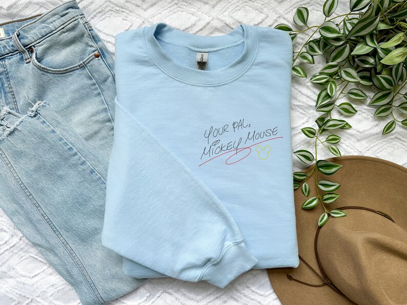 Puede incluir: Sudadera azul claro con el texto "Your Pal... Mickey Mouse" en escritura negra con una l&iacute;nea roja debajo y un icono de cabeza de Mickey Mouse amarillo.