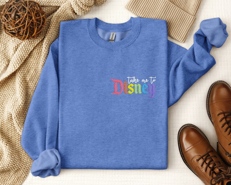May include: A blue sweatshirt with the text "Take me to Disney" in rainbow colours.