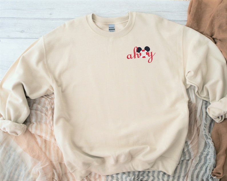 May include: A beige sweatshirt with a red embroidered design that says "ah-hy" with a Mickey Mouse head above the text.
