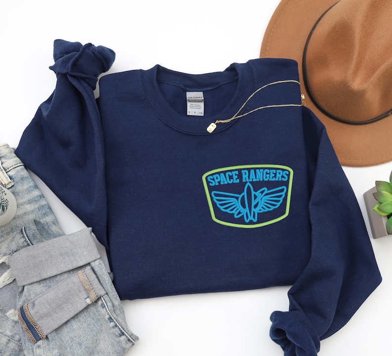 May include: Navy blue sweatshirt with a green and blue embroidered patch that says "SPACE RANGERS" with a rocket ship and wings inside the patch.