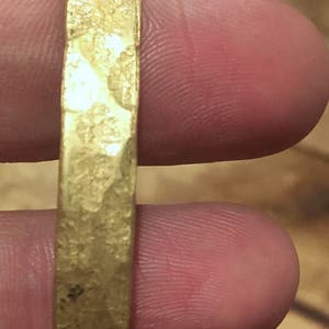 May include: A gold-colored metal bracelet with a hammered texture.