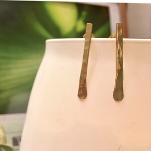May include: A pair of gold-toned hammered metal earrings. The earrings are long and thin, with a slightly rounded end.