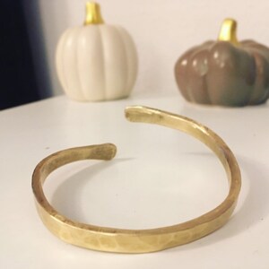 May include: A hammered brass bangle bracelet. The bracelet is a simple, minimalist design with a smooth, polished finish.
