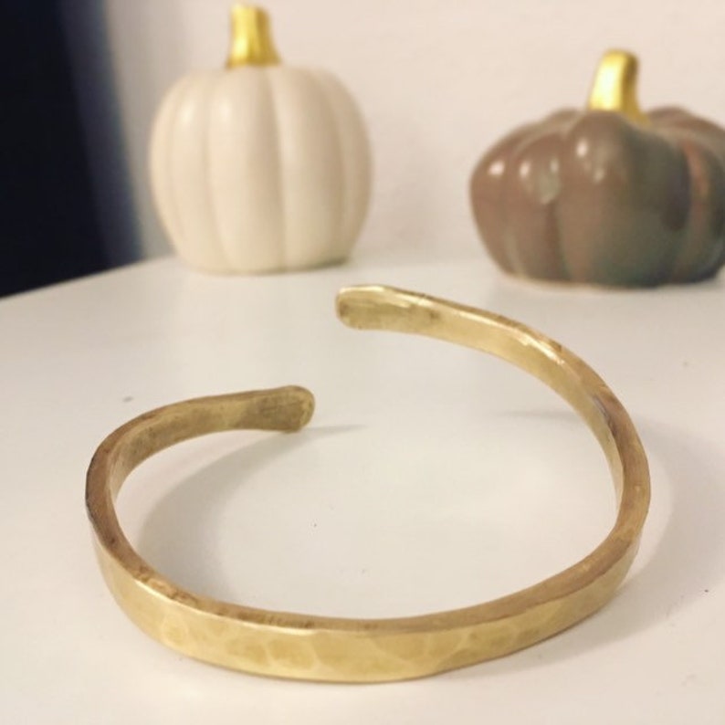 May include: A hammered brass bangle bracelet. The bracelet is a simple, minimalist design with a smooth, polished finish.