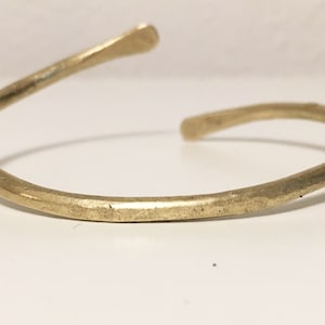 May include: A simple gold-toned metal bangle bracelet. The bracelet is made of a single piece of metal that is bent into a circle.