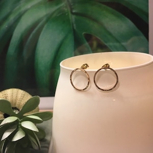 May include: A pair of gold-toned hoop earrings with a hammered texture. The earrings are small and delicate, and they are perfect for everyday wear.